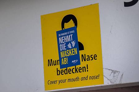 Ein Aufkleber mit der Aufschrift «Nehmt die Masken ab!» klebt über einem Schild, das zum Tragen einer Mund-Nasen-Maske auffordert. Die Mehrheit der Deutschen ist einer neuen Umfrage zufolge weiter für eine Isolationspflicht für Corona-Infizierte.